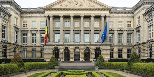 Vooraanzicht van het gebouw van het Federaal Parlement, met vooraan de strak gesnoeide hagen in de tuin.