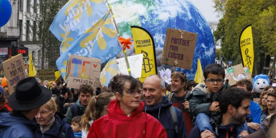 Een mensenmenigte demonstreert in de straten van Brussel. Verschillende mensen dragen vlaggen van Amnesty International en torsen een grote opblaaswereldbol. 