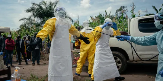 Hulpverleners, gekleed in felgele persoonlijke beschermingsmiddelen, een witte schort en een masker, worden met een product bespoten.