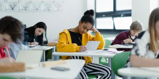 Een groep leerlingen in een klaslokaal schrijft in stilte in hun schriften. 