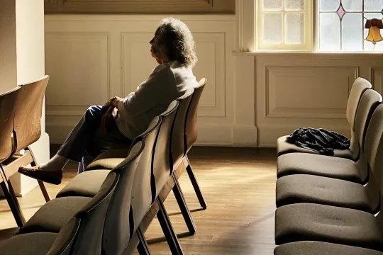 Persoon zit alleen op een rij stoelen in een door de zon verlicht gebouw.