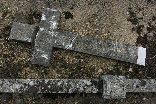 Een gebroken stenen kruis ligt op de grond.