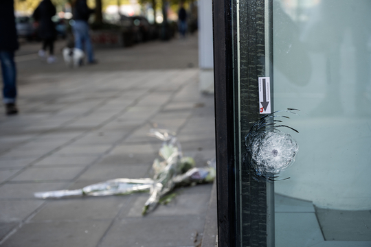 Een kogelgat in de glazen deur, met op de stoep twee bloemenruikers, op de plek waar op 16 oktober in Brussel twee Zweden werd neergeschoten door een Tunesische terrorist.