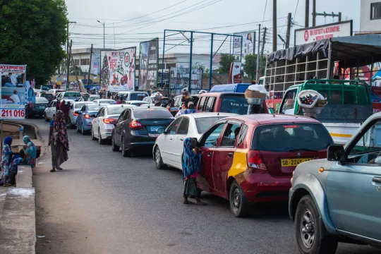 Een drukke straat in Accra, Ghana, waar mensen tussen filerijdende wagens wandelen.