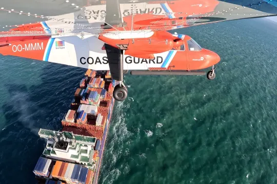 Zicht op een vliegtuig van de Belgische Kustwacht dat boven een containerschip vliegt.