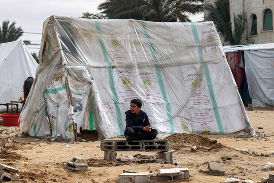 Een Palestijnse jongen zit op een betonblok voor een uit zakken geïmproviseerde tent in Rafah, in het zuiden van de Gazastrook.