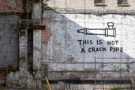 Graffiti 'This is not a crack pipe' op een muur nabij een braakliggend terrein verwijst naar roken van de drug crack.