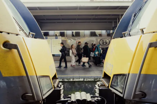 Tussen twee aan elkaar gekoppelde wagons zijn reizigers te zien op het perron.