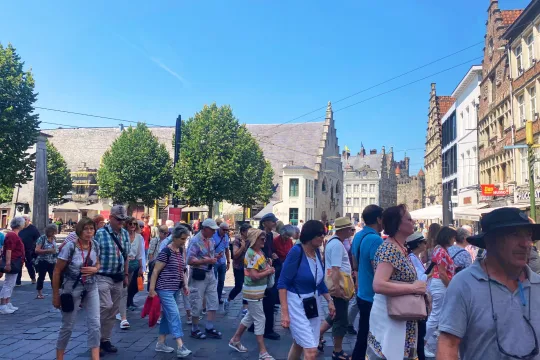 Een groep toeristen wandelt over de Groentenmarkt in Gent, op de achtergrond is het Groot Vleeshuis te zien.