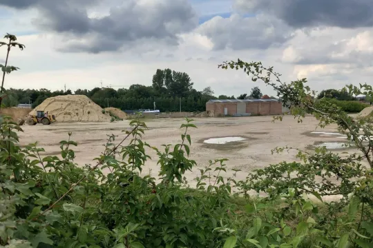 De terreinen van Grondwerken Paul Heylen in Lier, waarop een zandhoop en een graafmachine te zien is.