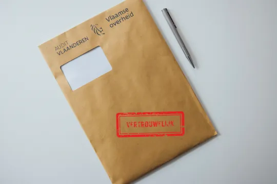 Een bruine envelop met daarop 'Audit Vlaanderen' en 'vertrouwelijk' op een wit oppervlak.