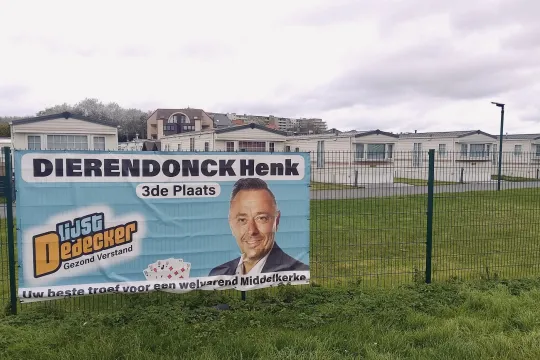 Een verkiezingsbanner voor Henk Dierendonck (Lijst Dedecker) hangt aan hek bij Camping Viking. Op de banner staat een foto van Dierendonck, met daarbij een waaier speelkaarten, de tekst '3de plaats' en de slogan 'Uw beste troef voor een welvarend Middelkerke'