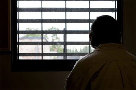 Beeld van een gedetineerde, gezien vanop de rug, die uit het raam kijkt van de gevangenis in Merksplas