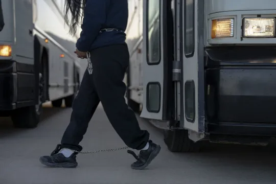 Een aan handen en voeten geboeide persoon stapt van een bus. De persoon wordt uit de Verenigde Staten gezet, via een militaire vlucht vanuit Fort Bliss in Texas.