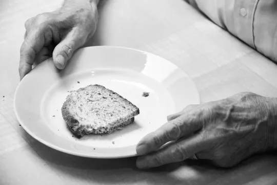 Zwart-wit foto van een oudere persoon die een boterham eet.