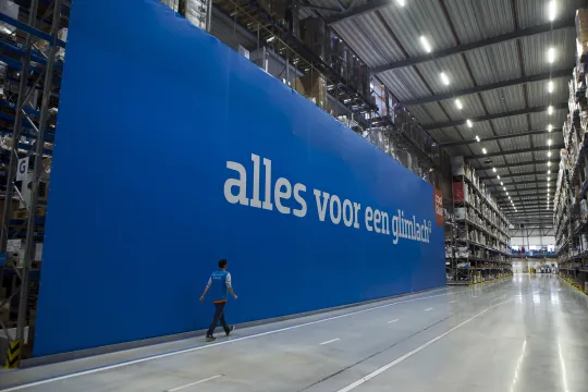 Een medewerker van Coolblue loopt voorbij een groot spandoek met de slogan 'alles voor een glimlach' in het distributiecentrum in Tilburg.