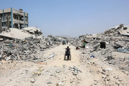 Een Palestijnse jongen trekt een rolstoel langs verwoeste gebouwen