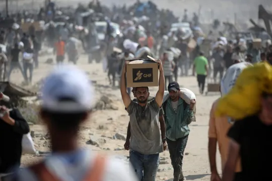 Een Palestijnse man draagt een doos terwijl anderen met tassen terugkeren van een voedseldistributiepunt dat wordt gerund door de door de VS en Israël gesteunde Gaza Humanitarian Foundation (GHF)-groep.