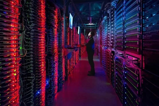 persoon kijkt naar een monitor in groot datacenter, gevuld met grote kasten met apparatuur voor digitale opslag
