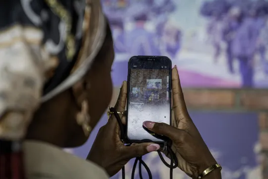 We kijken mee over de schouder met een studente die in Kinshasa met haar gsm een tentoonstelling fotografeert.
