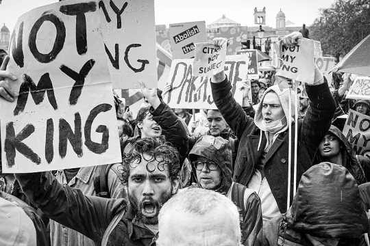 Zwart-wit beeld van betogers die bordjes met de tekst 'Not my king' in de lucht houden. 