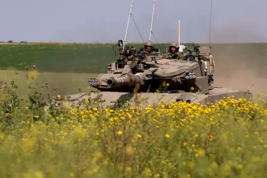 Een Israëlische tank rijdt door een natuur- en landbouwgebied met gele bloemetjes