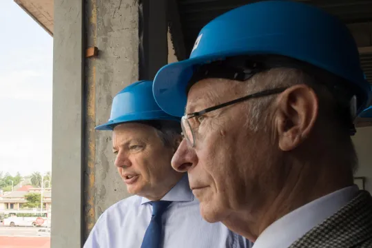 Didier Reynders (MR) en Jean-Claude Fontinoy kijken met een blauwe bouwvakkershelm uit het raam tijdens een werfbezoek