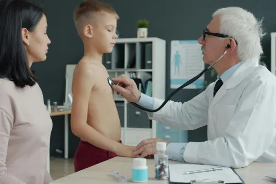Een dokter onderzoekt een jongetje, zijn moeder zit naast hem. 