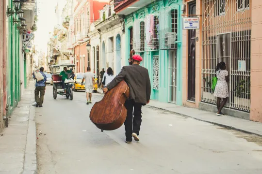 We kijken op de rug van een man die met een contrabas door de straten van Cuba wandelt.