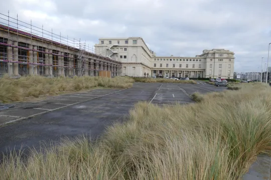Zijaanzicht van het Thermae Palace met op de voorgrond een grote lege parking.