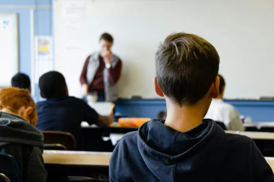 Achteraanzicht van een jongen die aan een schoolbank zit in een klaslokaal.