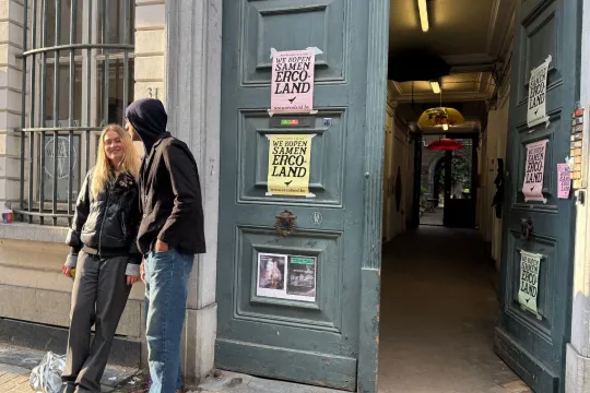 Twee mensen staan te praten voor de grote groene deur van kunstenaarshuis Ercola. Op de deur hangen posters van bugercoöperatie Ercoland.