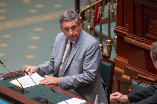 Jan Jambon, in een lichtgrijs kostuum, zit achter het spreekgestoelte in de Kamer. 