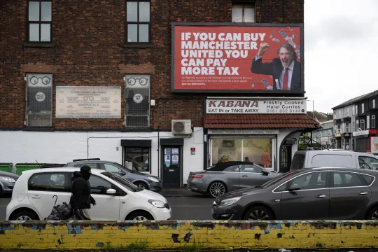 Een reclameposter met een afbeelding van Jim Ratcliffe, mede-eigenaar van Manchester United en CEO van chemieconcern INEOS, met de slogan "Als je Manchester United kunt kopen, kun je meer belasting betalen".