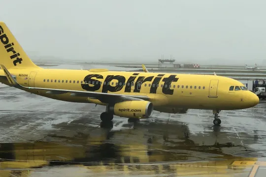Een geel vliegtuig met 'spirit' op de zijkant staat te wachten in een luchthaven. 
