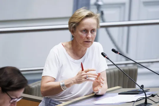 Annick De Ridder, met kort blond haar en in een wit t-shirt, spreekt het Vlaamse Parlement toe. 