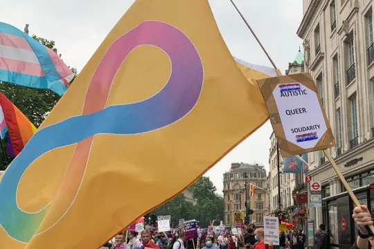 Een persoon (niet in beeld) houdt een grote Autistic Pride-vlag vast op een Pride-betoging. 