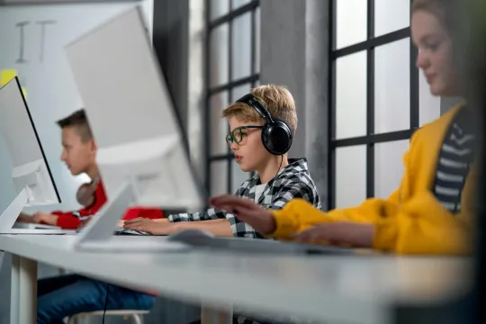 Drie jonge kinderen zitten in een klaslokaal achter computerschermen.