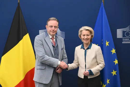 Bart De Wever en Ursula von der Leyen schudden elkaar de hand voor een Belgische en Europese vlag.