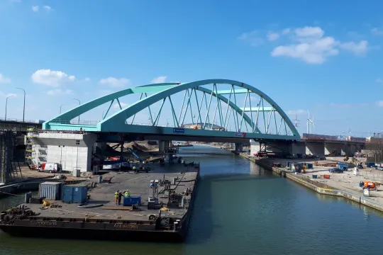 Een grote lichtblauwe brug wordt boven een kanaal geïnstalleerd.