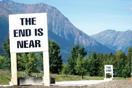 Een bordje met 'The end is near' voor een bergrijk landschap.