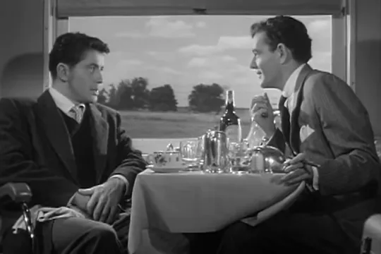 Zwart-wit filmstill uit 'Strangers on a train'. Twee mannen zitten te dineren in een trein. 