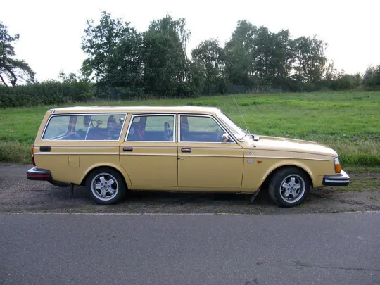 Een gele Volvo 245 voor een grasveld. 