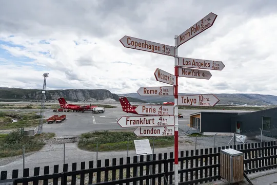 Afgelegen luchthaven in bergachtig gebied, met op de voorgrond richtingaanwijzers die de afstand tot een aantal grote steden tonen. 