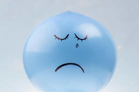 Blauwe ballon waar een huilende smiley op getekend is. 