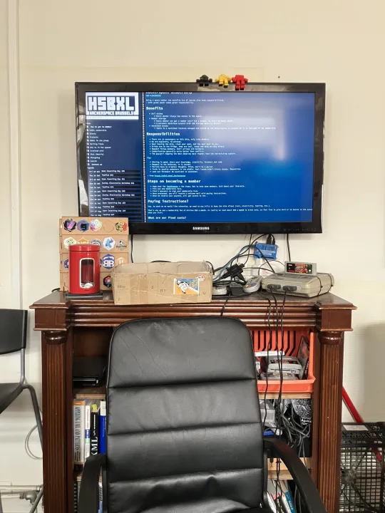 Op een computerscherm staat op een blauwe achtergrond het logo van HSBXL, de Brusselse hackerspace, en uitleg over de werking. Het scherm staat op een kast, met daarop onder meer ook een oude spelconsole. In de kast zitten verschillende computerspelletjes.