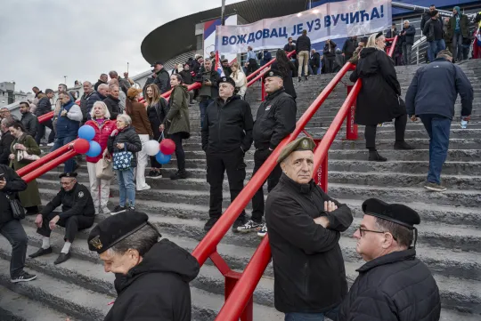 Mannen en vrouwen staan op trappen van een stadion, met wit-rood-blauwe balonnen en baretten.