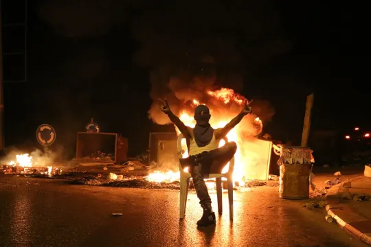 Een jongen zit op een stoel voor een vuurblokkade op de weg naar het dorpje Surida. Die moet voorkomen dat het leger het huis van een doodgeschoten Palestijn komt vernietigen. (Foto: Muhanned Darabee)