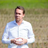 Jo Brouns staat, gekleed in een wit hemd, op een veld.