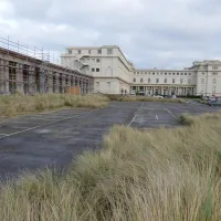 Zijaanzicht van het Thermae Palace met op de voorgrond een grote lege parking.